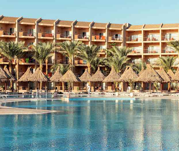 En hotelbygning med altaner, foran en pool og palmer. (AI-genereret tekst)