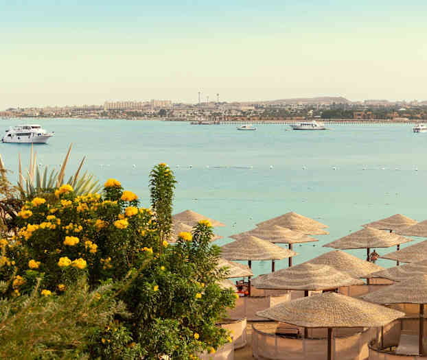 Strand med parasoller, havet og både i baggrunden. (AI-genereret tekst)