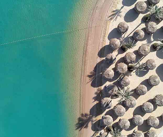 Luftfoto af en sandstrand med turkis vand og parasoller. (AI-genereret tekst)