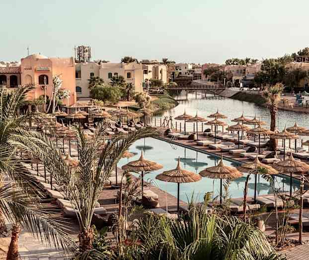 Poolområde med liggestole og parasoller, omgivet af palmer og bygninger. (AI-genereret tekst)