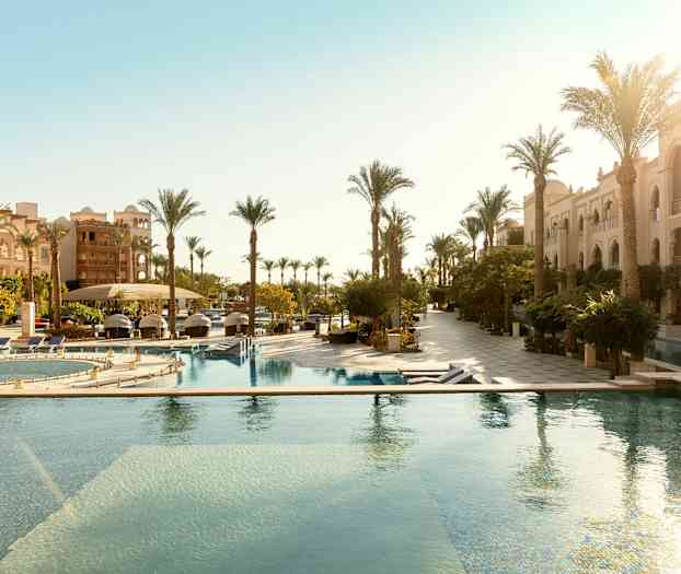 Hotelområde med udendørs pools og rækker af palmer ved siden af bygninger. (AI-genereret tekst)