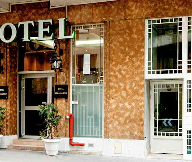 Forsiden af et hotel med et skilt, der siger 'Hotel Ambassadeur'. (AI-genereret tekst)