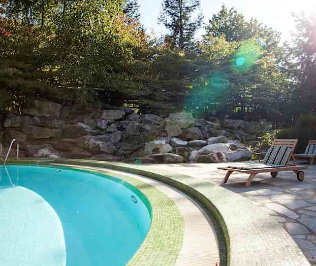 En pool omgivet af liggestole og grøn natur. (AI-genereret tekst)