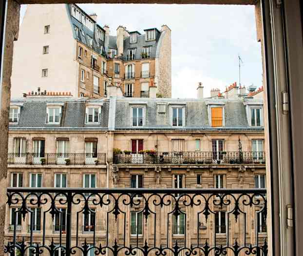 Et billede af en bygning med altaner taget fra et vindue med jerngelænder. (AI-genereret tekst)