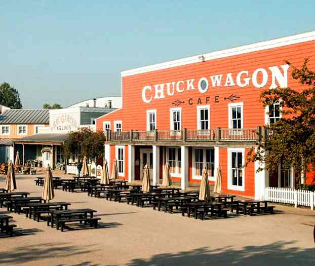 Et område med borde og parasoller foran en bygning med skiltet 'Chuck Wagon Cafe'. (AI-genereret tekst)