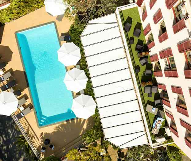 Billede af en pool, liggestole og parasoller ved siden af en bygning. (AI-genereret tekst)