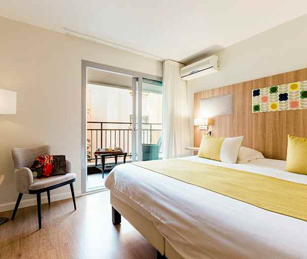 Et hotelværelse med en stor seng, en lænestol, et skrivebord og en altan. (AI-genereret tekst)