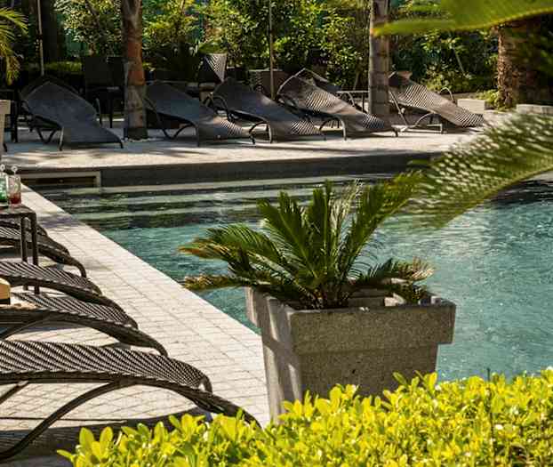 En udendørs pool med liggestole og planter i nærheden. (AI-genereret tekst)