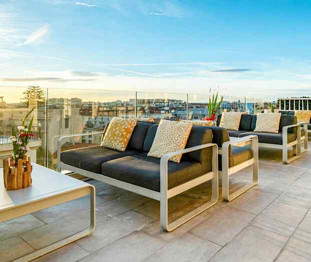 Møbleret tagterrasse med udsigt over byen og solnedgangen. (AI-genereret tekst)