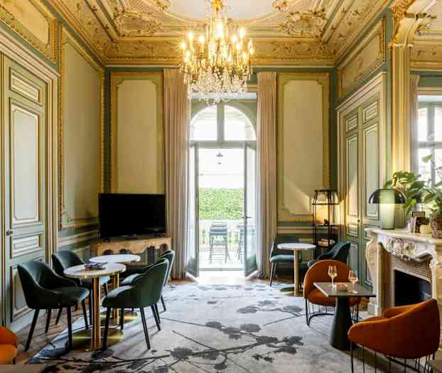 Et elegant møbleret rum med udsmykket loft, siddegrupper og en lysekrone. (AI-genereret tekst)