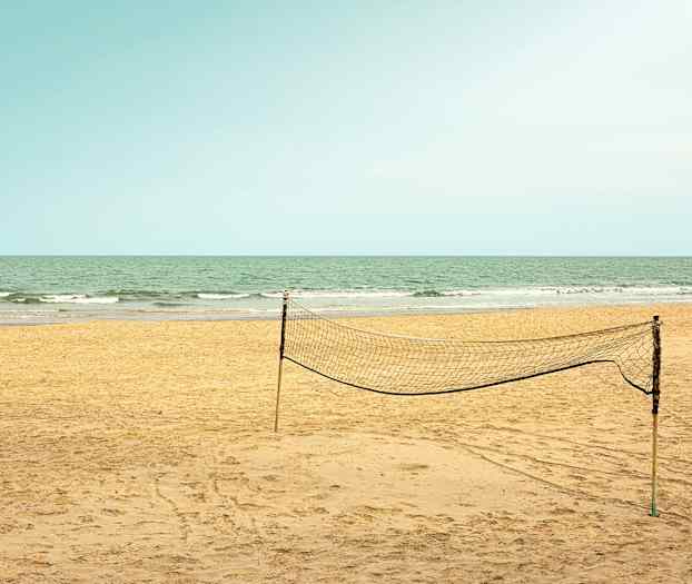 En tom sandstrand med et opstillet volleyballnet og havet i baggrunden. (AI-genereret tekst)