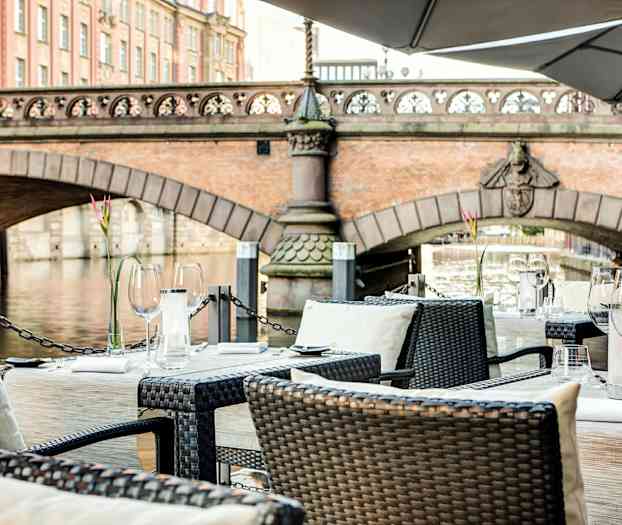 Velplacerede borde på en terrasse med udsigt over en bro og en flod. (AI-genereret tekst)