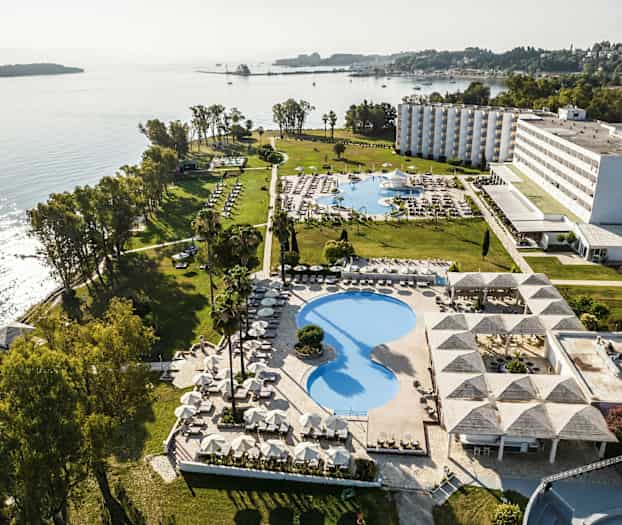 Luftfoto af et hotelområde ved havet med swimmingpools, grønne områder og bygninger. (AI-genereret tekst)
