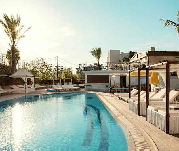 Billede af en udendørs swimmingpool omgivet af solsenge og palmer, med en klar blå himmel over. (AI-genereret tekst)