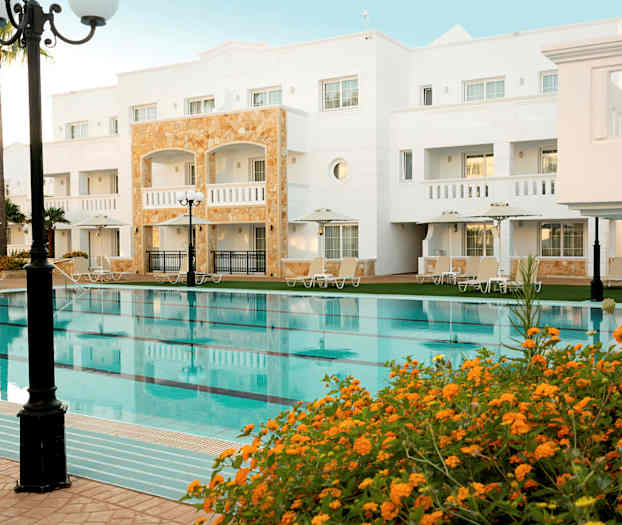 Hotelbygning med pool og omkringliggende solsenge. (AI-genereret tekst)