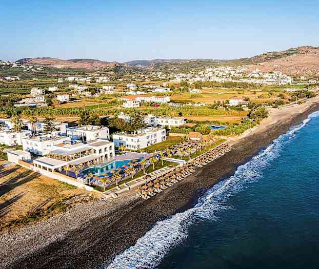 Udsigt over en strand med parasoller, liggestole og et resort med pools i nærheden. (AI-genereret tekst)