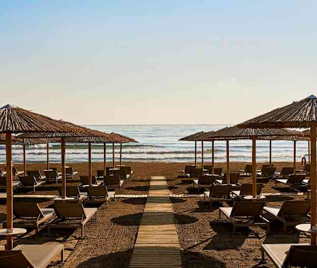 Liggestole og parasoller på en strand foran havet. (AI-genereret tekst)