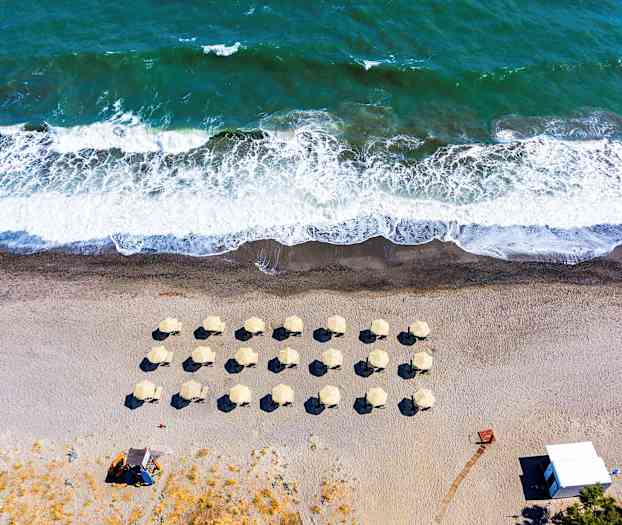 Luftfoto af en strand med parasoller og bølger. (AI-genereret tekst)