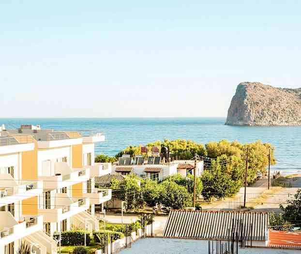 Udsigt over bygninger, grønt områder og havet med en klippe i baggrunden. (AI-genereret tekst)