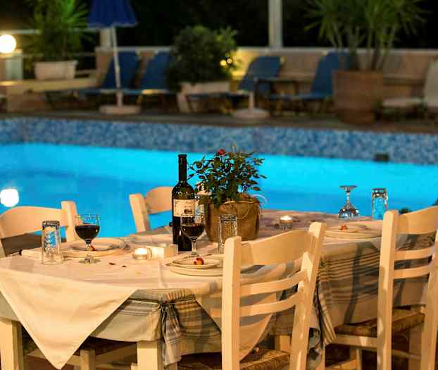 Et dækket bord med hvide stole ved siden af en oplyst pool. (AI-genereret tekst)