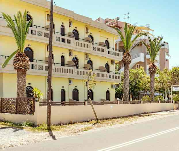 En gul bygning med flere etager og balkoner, omgivet af palmer og en vej. (AI-genereret tekst)