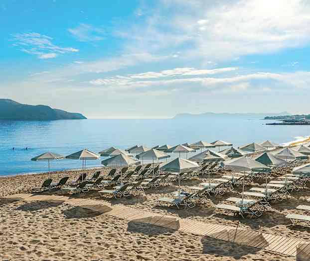 Udsigt over en strand med liggestole og parasoller, omgivet af hav og en fjern ø. (AI-genereret tekst)