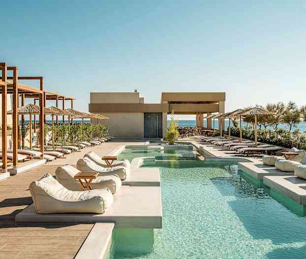 Udendørs pool med liggestole og parasoller langs kanten, med havet i baggrunden. (AI-genereret tekst)