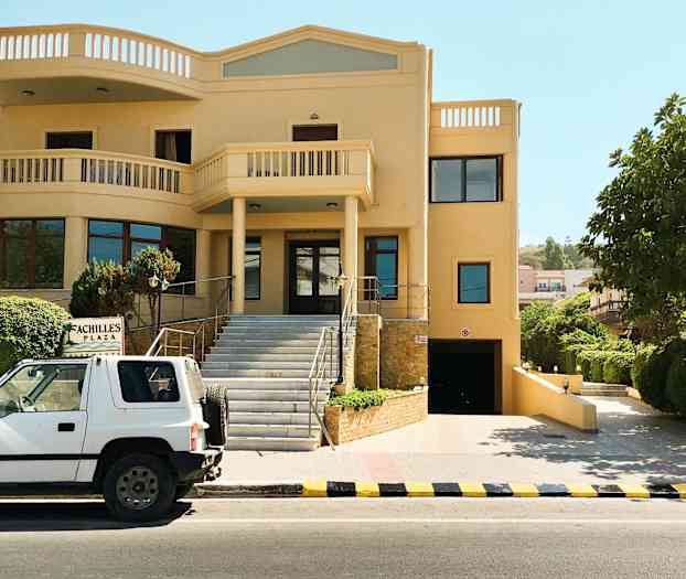 En bil er parkeret foran en bygning med et skilt med teksten 'Achilles Plaza'. (AI-genereret tekst)