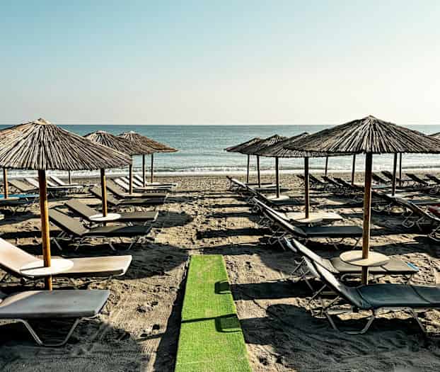 Strand med liggestole og parasoller på række ved havet. (AI-genereret tekst)