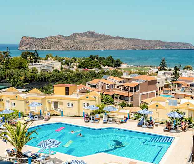 En pool med liggestole og parasoller foran en udsigt, der inkluderer huse, grønne områder og hav. (AI-genereret tekst)