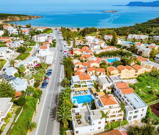 Luftfoto af en kystby med huse, pooler og hav i baggrunden. (AI-genereret tekst)