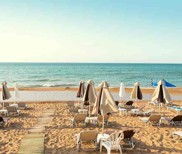 Liggestole og parasoller opstillet på en sandstrand med havet i baggrunden. (AI-genereret tekst)