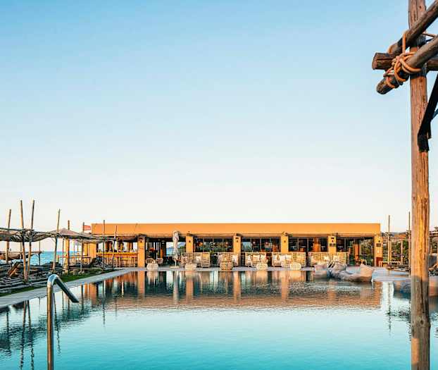 Billede af en pool med liggestole og et hus i baggrunden ved solopgang eller solnedgang. (AI-genereret tekst)