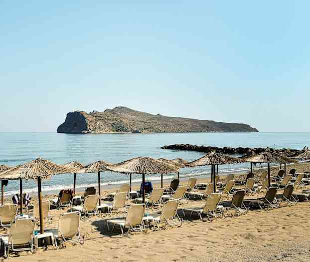 Liggestole og parasoller på en sandstrand med en klippe i havet. (AI-genereret tekst)