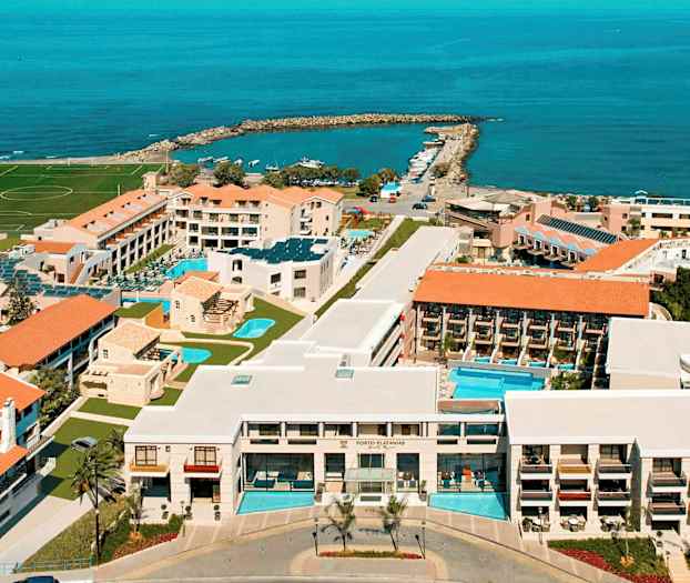 Luftfoto af et hotelkompleks ved kysten med swimmingpools, bygninger og havet i baggrunden. (AI-genereret tekst)