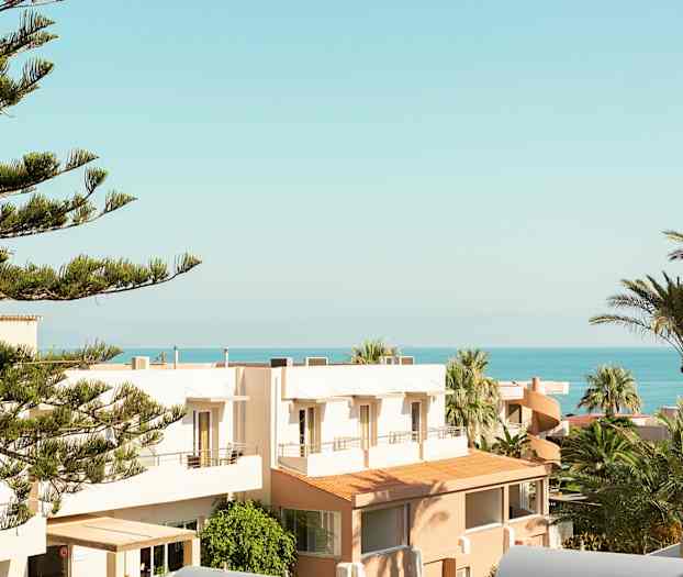 Udsigt over træer, bygninger og havet under en klar himmel. (AI-genereret tekst)