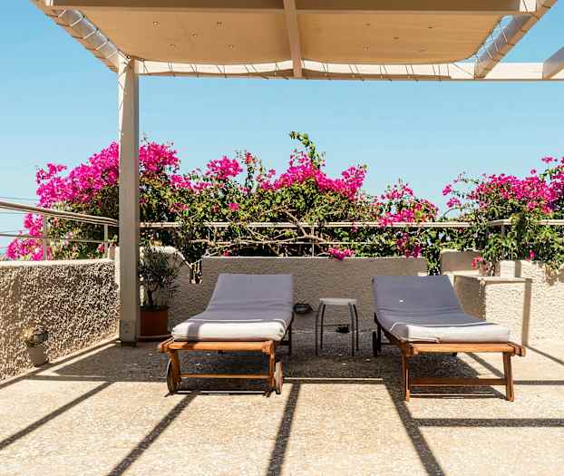 Terrasse med to liggestole, bougainvillea og overdækning under blå himmel. (AI-genereret tekst)