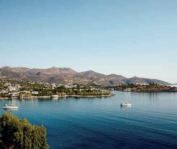 Landskab med en rolig bugt, sejlbåde og små bygninger ved foden af bjerge. (AI-genereret tekst)