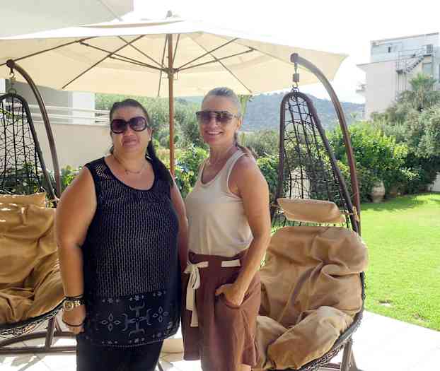 To hængestole står under en stor parasol på en terrasse med udsigt til en have og omkringliggende bygninger. (AI-genereret tekst)