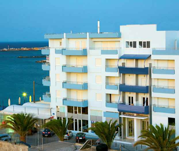 Lejlighedsbygning tæt på havet, omgivet af palmer. (AI-genereret tekst)