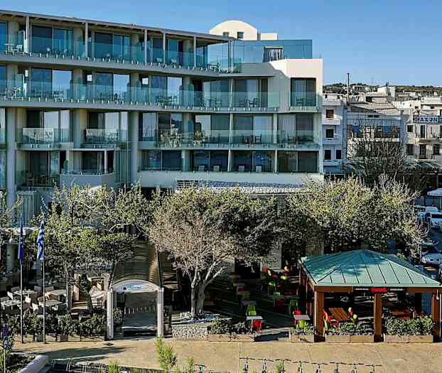 Et moderne hotel med altaner og en udendørs serveringsområde med siddepladser under tag og åben himmel, omgivet af træer. (AI-genereret tekst)