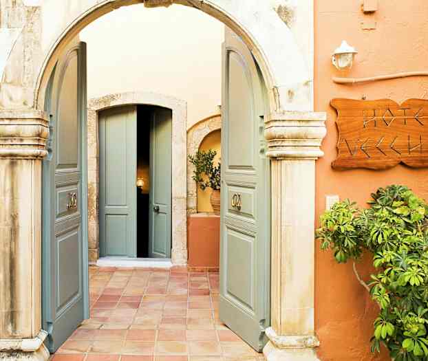 Billedet viser en indgang med en bue, åbne dobbeltdøre, et skilt med teksten 'Hotel Vecchio' og vegetation omkring. (AI-genereret tekst)