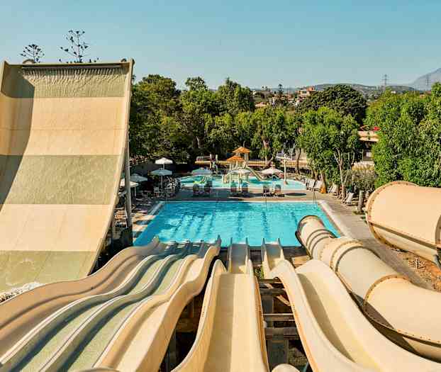 Billede af en vandpark med flere vandrutsjebaner, der fører ned til en pool omgivet af grønne træer. (AI-genereret tekst)