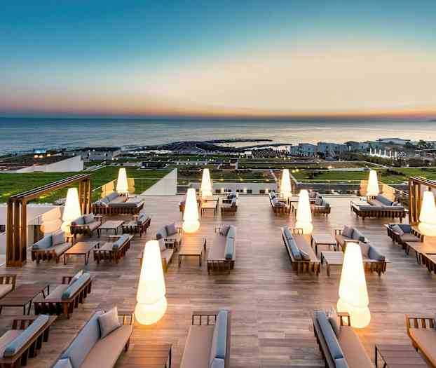 Moderne udendørsmøbler med oplyste lamper på en stor terrasse med havudsigt. (AI-genereret tekst)