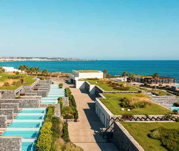 Udsigt over et ferieanlæg ved havet med private pools og grønne områder. (AI-genereret tekst)