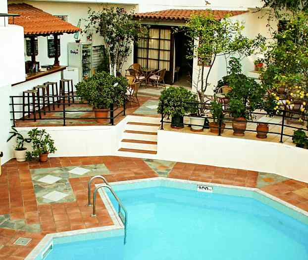 En udendørs pool med tilstødende spiseområde og bar, omgivet af grønne omgivelser. (AI-genereret tekst)