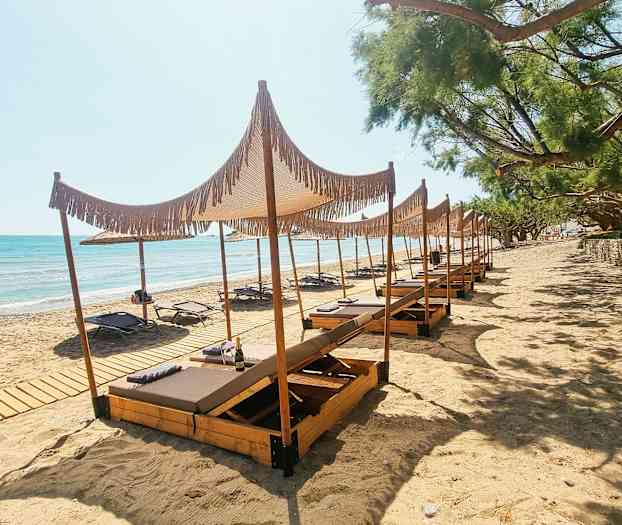 Billede af en sandstrand med liggestole og træparasoller. (AI-genereret tekst)