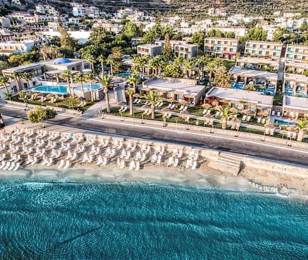 Luftfoto af en feriested ved stranden med parasoller og solsenge. (AI-genereret tekst)