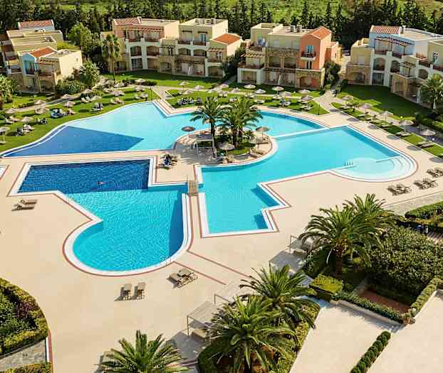 Udsigt over en stor udendørs swimmingpool omgivet af liggestole og parasoller med bygninger i baggrunden. (AI-genereret tekst)