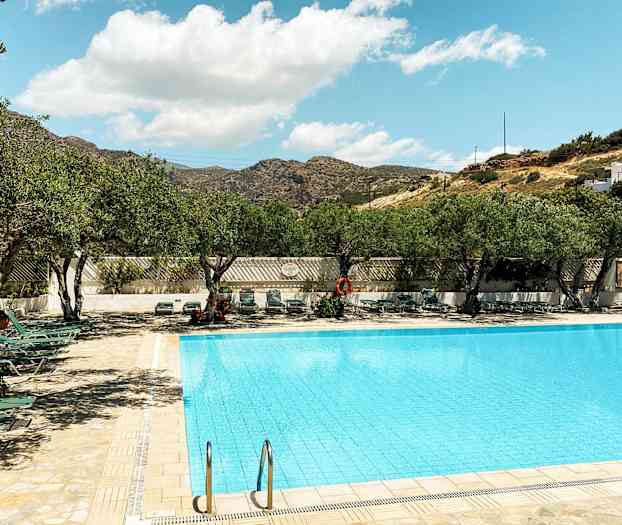 En udendørs pool omgivet af liggestole og træer under en klar himmel. (AI-genereret tekst)